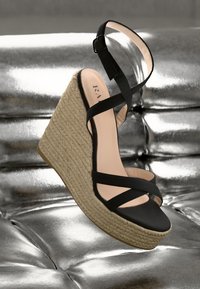 Schwarze Keilsandalen mit überkreuzten Riemen, Espadrille-Style Jutesohle und einer glatten, lederähnlichen Oberfläche. Mit einer Schnalle für einen sicheren Halt.