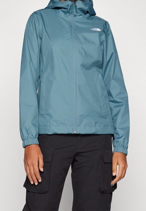 Veste légère à capuche turquoise, avec une texture lisse, fermeture éclair avant, poignets élastiques, poches latérales, et logo sur la poitrine.