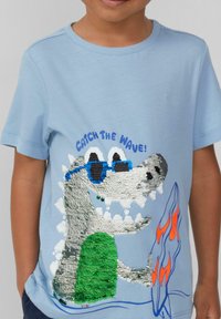 Hellblaues Baumwoll-T-Shirt mit einem mit Pailletten verzierten Krokodil-Graphic, das Sonnenbrillen trägt, sowie Flammen- und Wellenmustern in Orange und Grün.