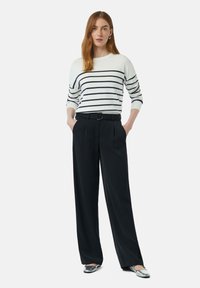 Gestreifter Pullover in Weiß und Marineblau mit Dreiviertelärmeln, kombiniert mit schwarzen weit geschnittenen Hosen und silbernen Slippern.
