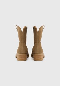 Stivali western in suede color sabbia con bordo scallop, chiusura con zip e tacco in legno impilato, caratterizzati da una superficie liscia e hardware minimale.