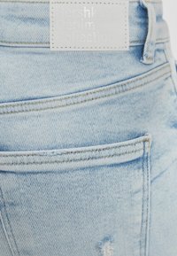 Ljusblå denimjeans med en synlig bakficka och en vit etikett med texten "Bershka Denim Collection" i upphöjd skrift.