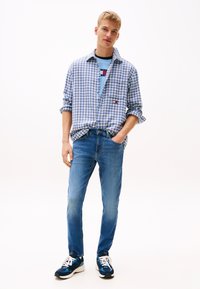 Chemise à carreaux bleus et blancs, T-shirt bleu clair, jean bleu et baskets bleues avec des accents blancs et des lacets.