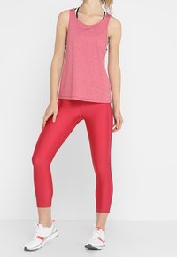 Leggings deportivos rojos combinados con una blusa sin mangas rosa jaspeada. El material es elástico, con un corte holgado y sin patrones visibles.