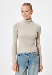 Maglione beige a collo alto con costine, maniche lunghe, design aderente e texture morbida abbinato a jeans in denim azzurro chiaro.
