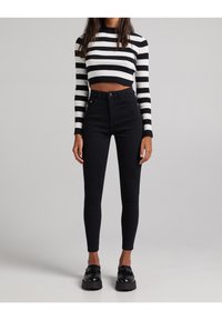 Černé vysoké skinny džíny spojené s černobílým proužkovaným zkráceným svetrem s žebrovanou texturou a dlouhými rukávy.