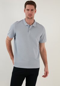 Světle modré polo tričko vyrobené z prodyšného materiálu s texturovaným vzorem, krátkými rukávy a zapínáním na tři knoflíky. Nosit s tmavými kalhotami.