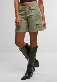 Olivenfargede cargo shorts med sidelommer og rett snitt, kombinert med knelange svarte lærboots med spiss tå.