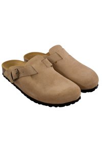 Zuecos de ante beige sin talón con hebilla lateral ajustable y suelas texturizadas negras, mostrados en vista de par lado a lado.