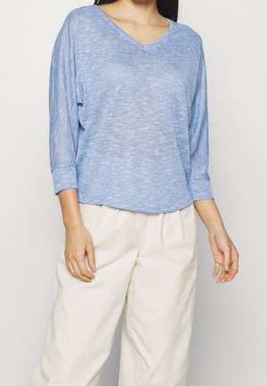 Haut bleu clair à manches longues avec col en V, fabriqué en tissu texturé, associé à un pantalon ample de couleur crème. Design simple et décontracté.