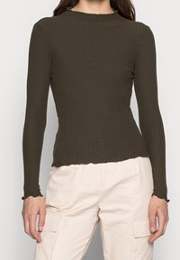 Haut à manches longues côtelé vert olive avec un col haut, doté de poignets délicatement festonnés et d'un ourlet légèrement cropé.