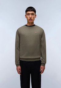 Sudadera verde oliva con cuello redondo y mangas largas; cuenta con un pequeño emblema de bandera roja y blanca en el pecho. Textura suave de algodón.