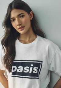 Balta kokvilnas T-kreklā ar lielu melnu grafiku, uz kuras ir rakstīts "oasis" treknā fontā,  ar apļveida kakla izgriezumu un brīvu piegriezumu.