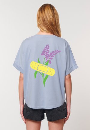 Una persona que lleva una camisa azul con una vendaje amarillo y un gráfico de flores moradas en la parte de atrás, combinada con pantalones cortos negros.