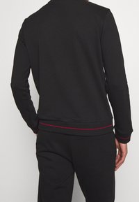 Schwarzer Pullover mit Rundhalsausschnitt, langen Ärmeln und roten Akzenten an Saum und Nähten, mit glatter Textur und tailliertem Design.