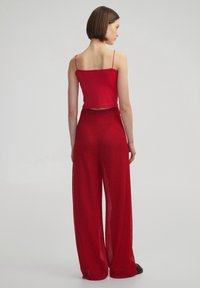 Top corto rosso con spalline fini abbinato a pantaloni larghi rossi e texture. Il tessuto è leggero e presenta un motivo a maglia.