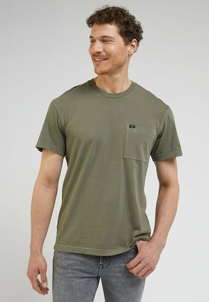 Camiseta de algodón verde oliva con cuello redondo, mangas cortas y un bolsillo en el pecho que incluye una pequeña etiqueta de la marca.