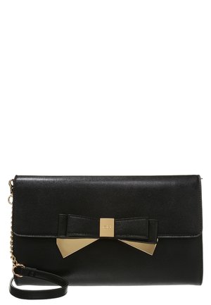 Black leather clutch bag with a gold-tone bow accent and detachable wrist strap, featuring a flap closure and a chain detail on the side.