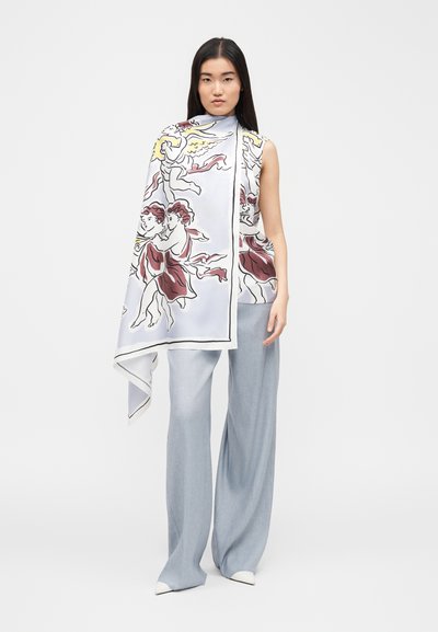 Γυναίκα που φοράει ανοιχτό μπλε παντελόνι με φαρδιά πόδια και αμάνικο τοπ, με ένα μεγάλο φουλάρι με θέμα αγγέλου να πέφτει ασύμμετρα πάνω από τον έναν ώμο.