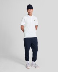 Hvit polo med blå detaljer, logo på brystet; marineblå joggebukser; grå sneakers; ribbet marineblå lue; avslappet antrekk vist på en person.