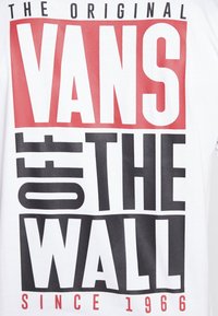 Rohkeaa tekstiä slogan "The Original Vans Off The Wall Since 1966" punaisena, mustana ja valkoisena valkoisella kankaalla.