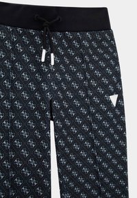 Svarta joggingbyxor med ett upprepat mönster av ljusblå logotyper, elastisk midja och snörning, med en vit triangulär accent.