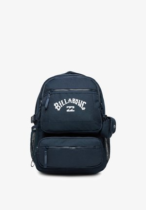 Dark blue Billabong backpack with multiple zippered compartments, mesh side pockets, and a small attached pouch on the side.