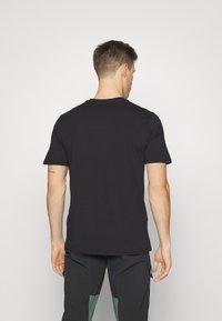 Bageste udsigt af en sort bomulds t-shirt med rund hals og korte ærmer, der har en glat tekstur og minimale sømme.