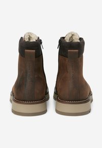 Stivali ankle in pelle marrone con una morbida fodera in pile, colletto in suede scuro e chiusura con zip. Presentano una suola in gomma spessa e cuciture in contrasto.