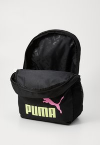 Juodas audinio kuprinė su uždengimu, pasižyminti dideliu gelsvu „PUMA“ logotipu ir rožiniu pumos siluetu. Viduje yra raštuota juoda pamušalas.