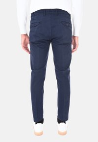 Pantaloni di cotone blu navy con una vestibilità slim, dotati di due tasche posteriori e una texture liscia, abbinati a sneakers bianche.