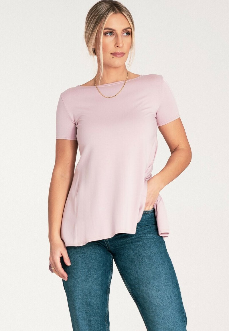 Jasnoróżowa bluzka z krótkim rękawem o okrągłym dekolcie, miękka w dotyku i luźna, w zestawieniu z dżinsami o średnim odcieniu.