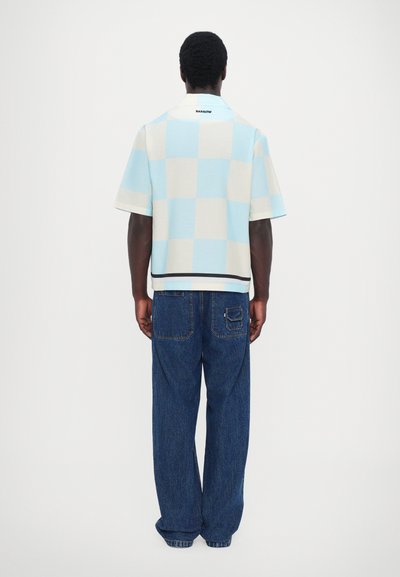Camisa de cuadros de manga corta en azul claro y crema, con cuello y un dobladillo negro en contraste, combinada con unos vaqueros azules de corte holgado.