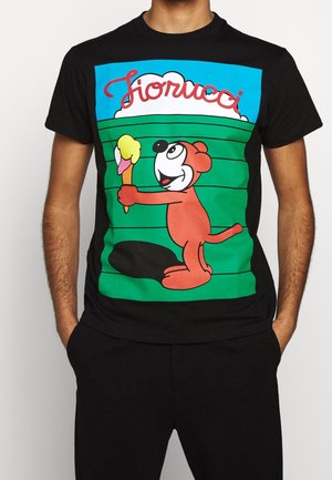 Kreskówkowy niedźwiedź trzymający rożek lodowy na czarnej koszulce z zielonym i niebieskim tłem oraz czerwonym tekstem "Fiorucci" powyżej.