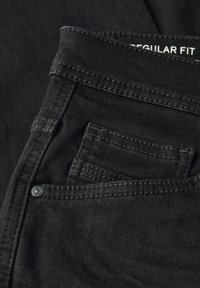 Primer plano de un bolsillo de jeans de mezclilla negra con costuras visibles, un remache y una etiqueta parcial que dice "AJUSTE REGULAR".