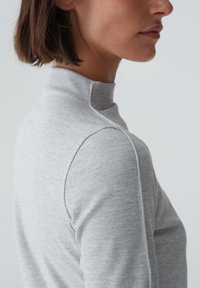 Grijze nep-turtleneck top gemaakt van ribbelstof, met een aansluitende vorm en subtiele naaddetails langs de schouders.