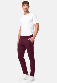 Burgunderfarbene Slim-Fit-Hosen mit Seitentaschen, kombiniert mit einem schlichten weißen T-Shirt und weißen Sneakern. Glatter Stoff und maßgeschneiderte Passform.