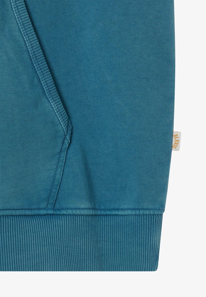 Skarpetka w kolorze niebiesko-skalnym z widocznymi szwami, prążkowanym dołem i małą beżową metką po prawej stronie z napisem "BLK WVS".