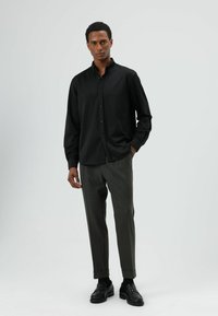 Zwart shirt met lange mouwen en knopen, gecombineerd met donkergrijze, op maat gemaakte broek en zwarte loafers. Eenvoudig, strak ontwerp met een ontspannen pasvorm.