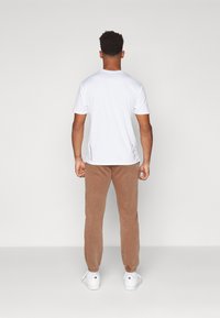 Hvid kortærmet t-shirt og lysebrune tapered sweatpants med elastiske manchetter og hvide sneakers, set bagfra.