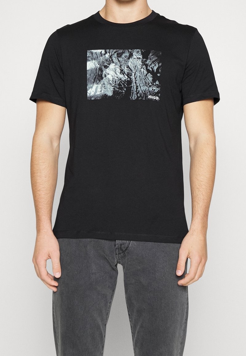 T-shirt en coton noir avec une grande impression graphique abstraite grise à l'avant. Col rond et manches courtes. Design simple.
