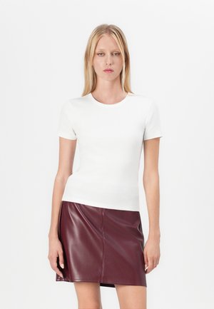 White ribbed short-sleeve top paired with a burgundy faux leather mini skirt. Smooth texture, round neckline, and fitted silhouette.