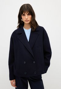 Námorně modrá dvouřadá bunda z vlněné směsi s velkými knoflíky, klopami a bočními kapsami. Disponuje uvolněným střihem a jemnou texturou.
