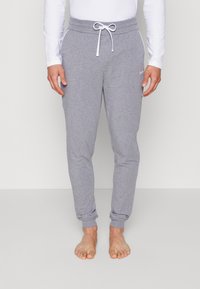 Grå joggebukser laget av mykt stoff med snor i livet, innsnevring ved bena og hvite detaljer på lommene.