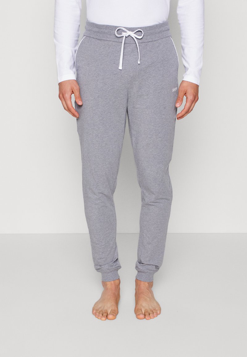 Grå joggebukser laget av mykt stoff med snor i livet, innsnevring ved bena og hvite detaljer på lommene.
