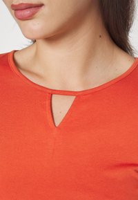 Red cotton top with a short, rounded neckline featuring a small keyhole cutout. Smooth texture and fitted design.