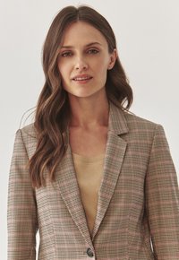 Blazer à carreaux légèrement structuré dans des tons beige, brun et rose, avec un col cranté, une coupe cintrée et une fermeture à bouton unique.