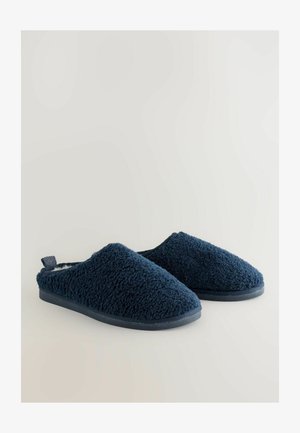 Granatowe kapcie o teksturowanej, puszystej powierzchni, miękkim wnętrzu i płaskiej, elastycznej podeszwie; zawierają pętelkę z tyłu.