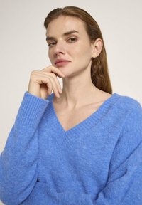 Hellblaues V-Ausschnitt-Pullover aus weichem, texturiertem Stoff. Mit gerippten Bündchen und einem lockeren Schnitt.