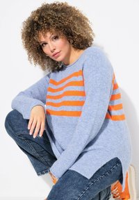 Maglione azzurro chiaro con strisce orizzontali arancioni, texture morbida, scollatura rotonda e maniche lunghe, abbinato a jeans in denim scuro.